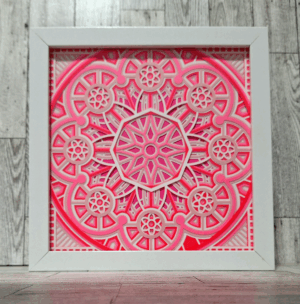 Layers of cut paper in shades of pink in a white frame.