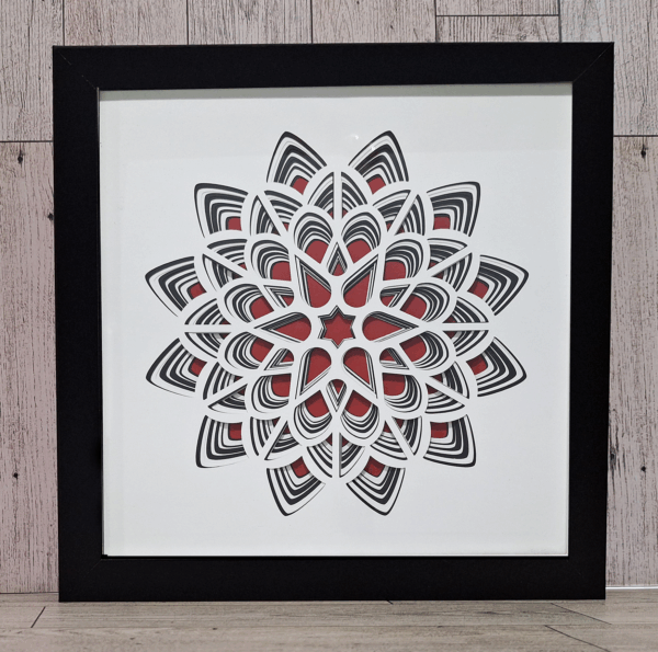 Layered paper in red, white, and black in black frame.