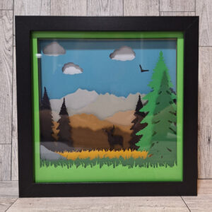 Mountain scene of layered paper with pine trees.